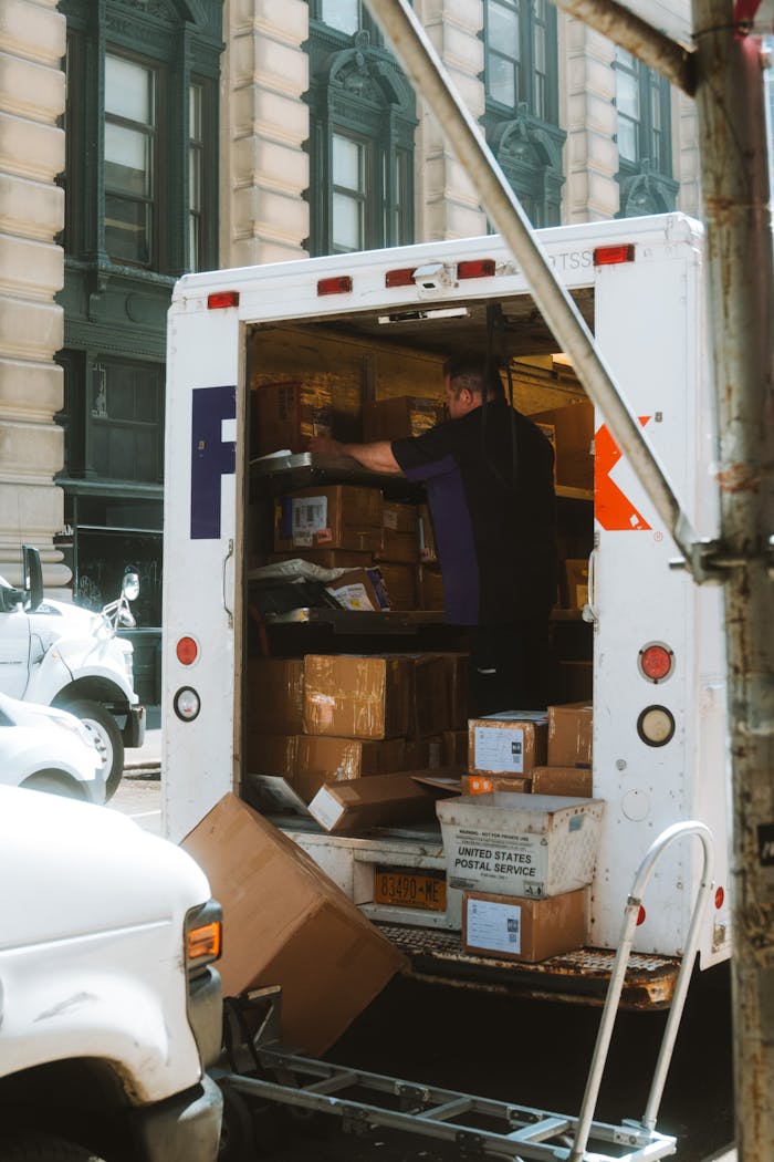 A delivery driver sorts packages in a truck on a busy urban street.