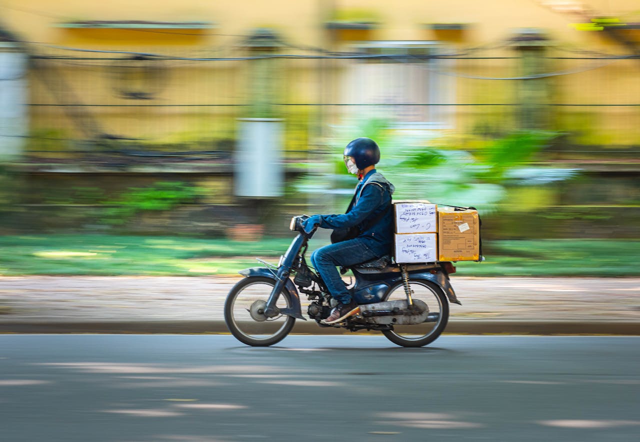 Side view of a motorcycle courier speeding down a road with packages in motion blur background.