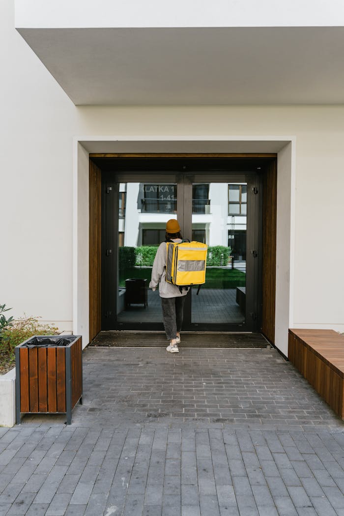 A food courier carrying a thermal bag enters a modern apartment building, ready for delivery.